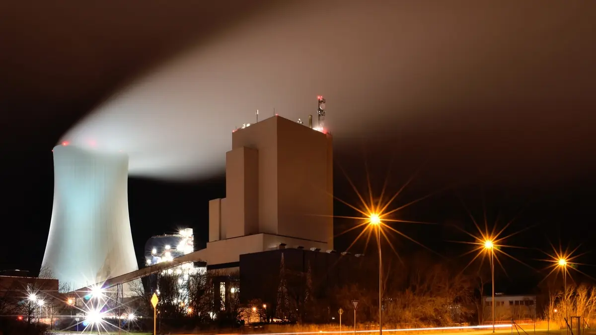 Night view of the Rostock power station in Germany, its cooling tower releasing a long plume of water vapour