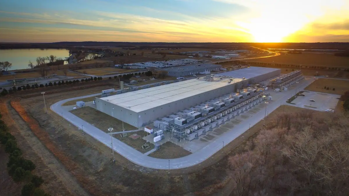 Aerial view at sunset of an existing hyperscale data centre in Council Bluffs, Iowa, with rows of cooling and backup power units along the building