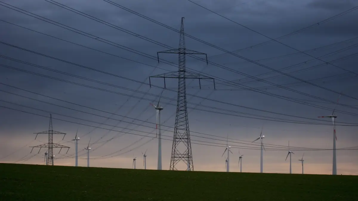 High-voltage pylons and overhead lines crossing a wind farm under an overcast evening sky near Nauen, Brandenburg, Germany.