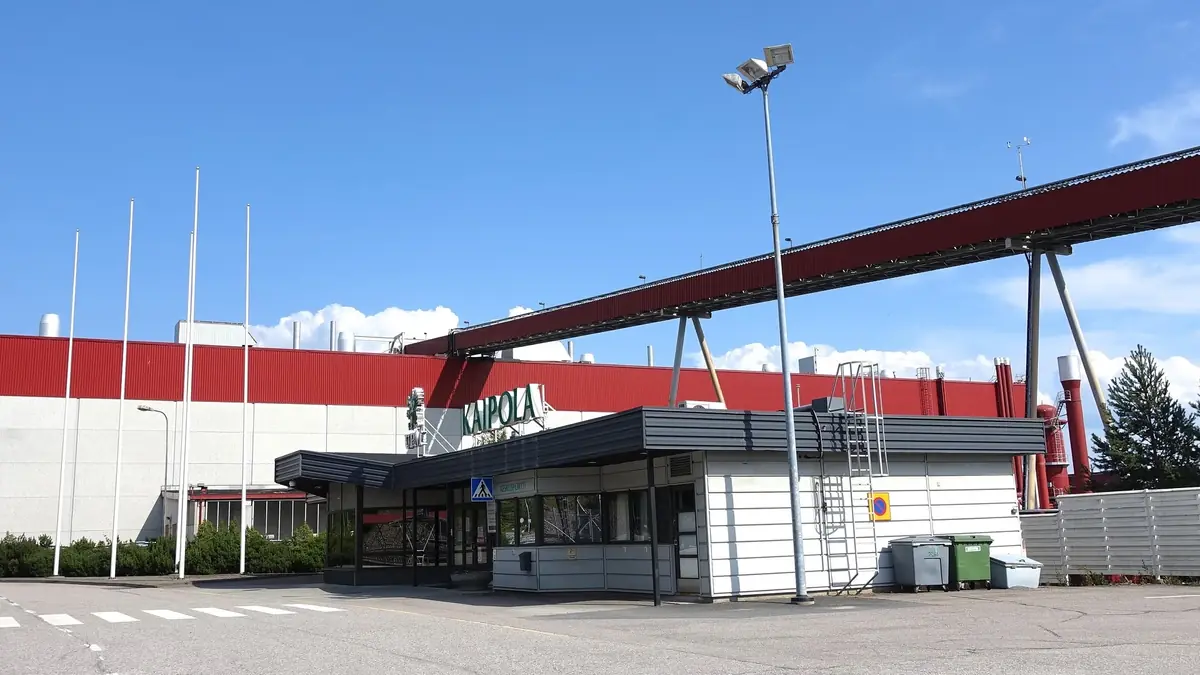 Gatehouse of the Kaipola paper mill in Jämsä, Finland, in July 2021: a long red and white mill hall behind the entrance, with a red conveyor bridge running above it.